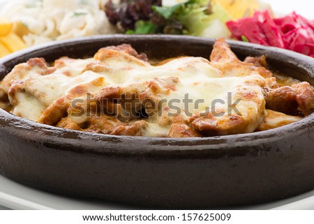 Cheese melted on chicken casserole in terracotta plate with salad and pasta on the side