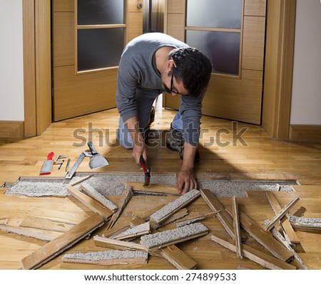 Manual worker disassembling wooden floor ruined from moisture and water leak