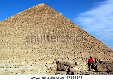 Girl in red exploring Egyptian pyramid on sky background