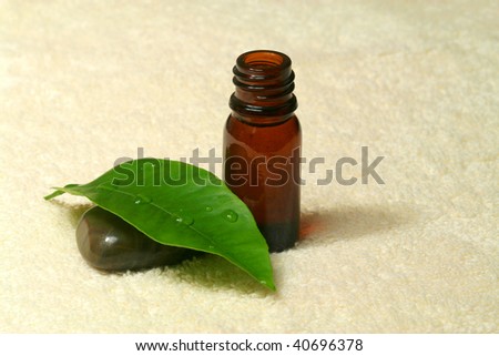 Essential orange oil in brown bottle, pebble and green orange leaf with droplets on cream towel