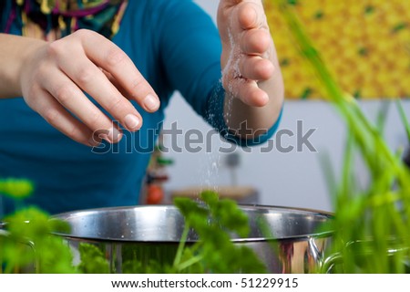 Woman salting a meal in a pot behind of herbs, parsley and chives