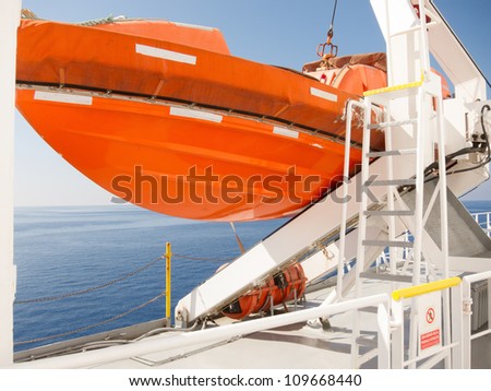 View out to sea of an orange lifeboat on deck of cruise ship suspended from a heavy metal davit