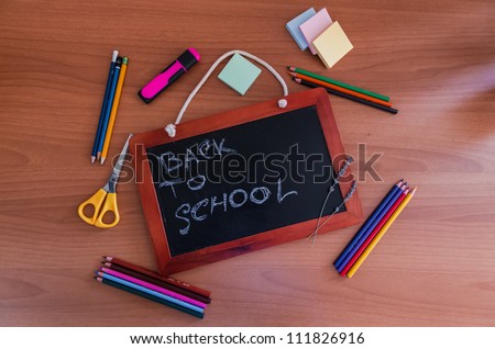 Small slate blackboard with the words Back to School surrounded by pencils, crayons, scissors and stationery