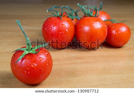 Tomatoes with stems on a wooden table in very dim light.