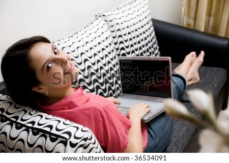 Smiley woman with laptop sitting on couch looking back