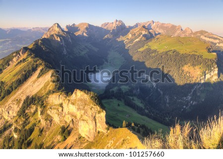 deep green valley with lake and mist floating on it and houses surrounded by high,steep, rocky mountain walls at Saentis, Switzerland