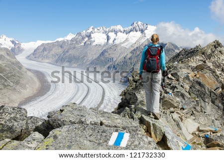 concept for hiking, climbing, walking and outdoor adventures: woman on mountain top with backpack and sticks above Aletsch glacier Switzerland
