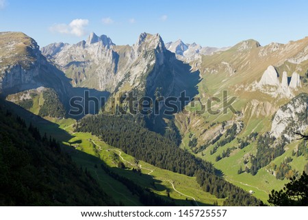 deep green valley with houses and road surrounded by high,steep, rocky mountain walls at Saentis, Switzerland