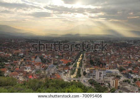 city scape of second biggest city Prizren in Kosovo at sunset with red roofed houses and mosques and river. In the background a mountain range.