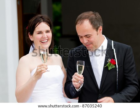 newly wed couple with wedding gown and dark suit: groom and bride toasting with champagne and enjoying the party
