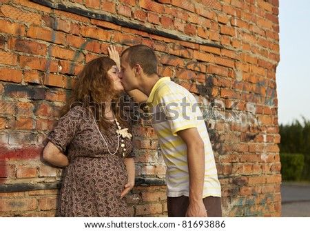 Portrait of a happy young man kisses his pregnant wife . outdoor .