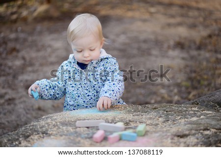 Adorable toddler girl playing with sidewalk chalk at spring