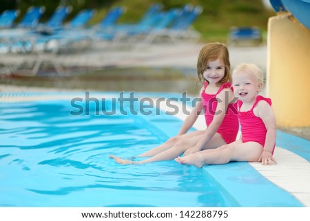 Two little sisters sitting by a swimming pool