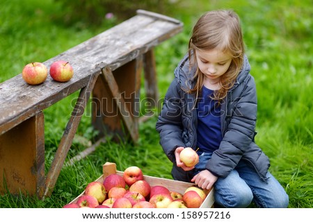 Little girl eating an apple by a wooden bench on autumn day