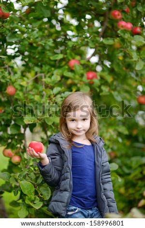 Little girl with an apple by an apple tree on autumn day
