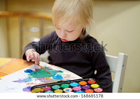 Cute toddler girl is drawing with paints in preschool
