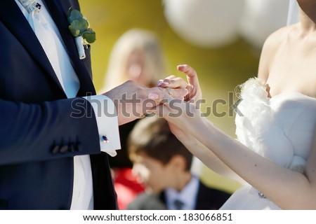 Bride is putting wedding ring on groom\'s finger