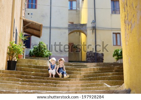 Two cute little sisters sitting on stairs in italian town