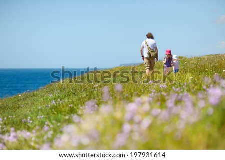 Two little sisters and their father hiking on a flower field by the sea