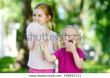 Adorable little sisters eating candy-floss outdoors at summer