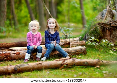 Two little sisters sitting on a big log in a forest