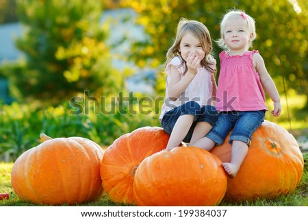 Two little sisters sitting on huge pumpkins on a pumpkin patch