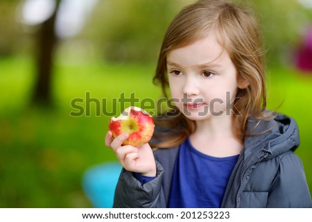 Cute little preschooler girl eating an apple on beautiful autumn day