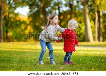 Two little sisters hugging each other in beautiful autumn park on a sunny day