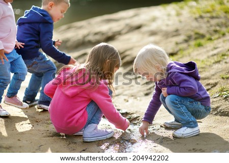 Three little sisters and their brother playing by a river on beautiful sunny autumn day