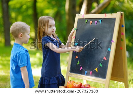 Adorable little girl playing a teacher standing by a blackboard in front of her little student