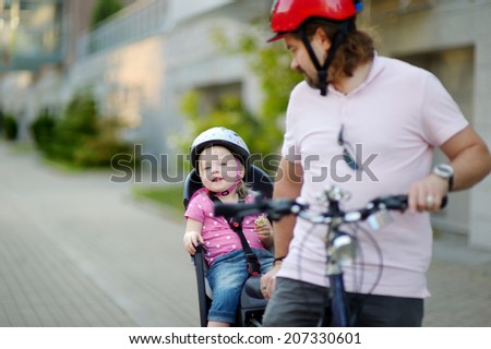 Young father and his cute little toddler daughter in a child seat getting ready to ride a bicycle