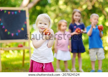 Four adorable little kids holding healthy organic apples in summer park on beautiful sunny day