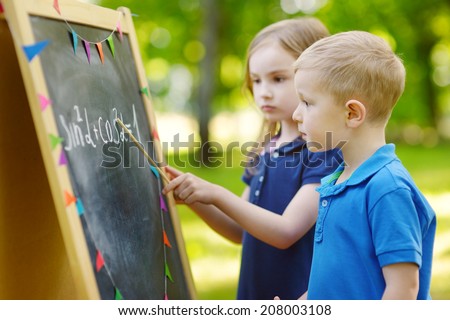 Adorable little girl playing a teacher standing by a blackboard in front of her little student