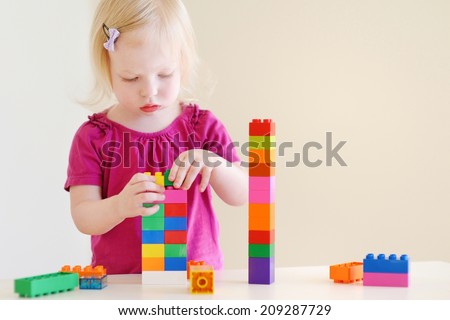 Cute little toddler girl playing with colorful plastic blocks at home