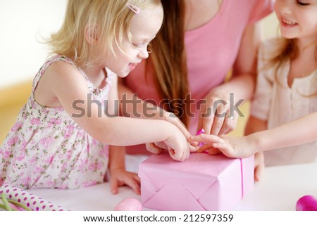 Young mother and her two little daughters wrapping a gift with pink wrapping paper