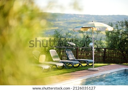 Round beige sunshade and several folding beach chairs by the outdoor pool in agriturismo overlooking green fields and farmlands of Tuscany, Italy. Foto d'archivio © 