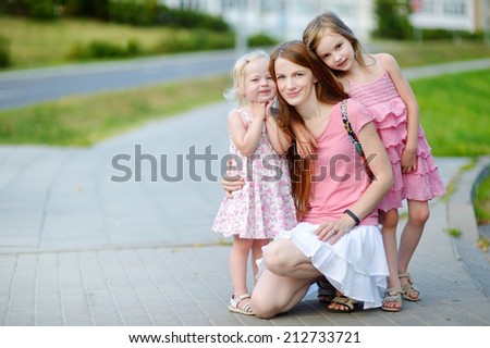 Young beautiful mother and two little daughters hugging in summer park on warm and sunny day