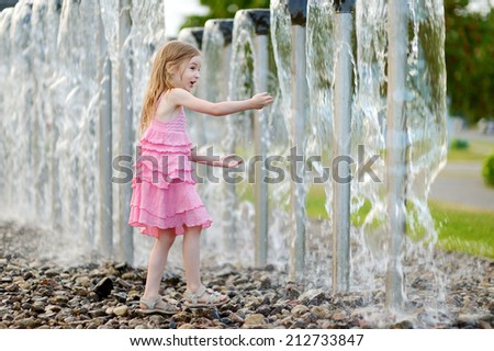 Cute little preschooler girl playing with a city fountain on hot and sunny summer day