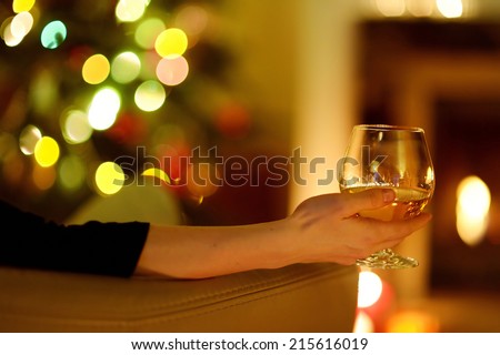 Woman having a drink by a fireplace in a cozy dark living room on Christmas eve