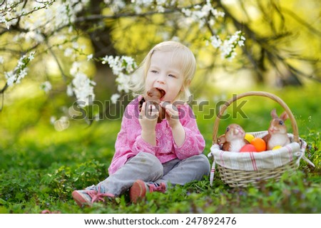 Adorable toddler girl eating chocolate bunny in a spring garden on Easter day
