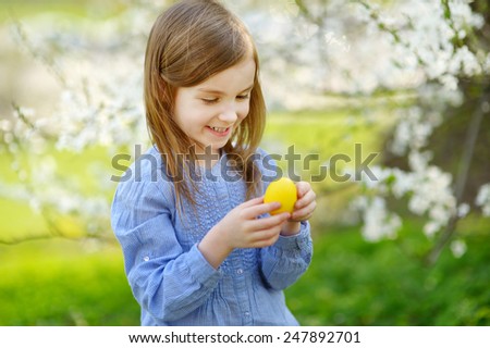 Adorable little girl playing with Easter egg in blooming spring garden on Easter day