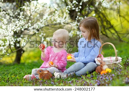Two adorable little sisters playing with Easter eggs in blooming spring garden on Easter day