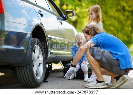 Young father and his two daughters changing a car wheel outdoors on beautiful summer day