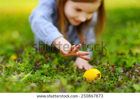 Adorable little girl hunting for easter egg in blooming spring garden on Easter day