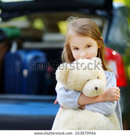 Adorable little girl with big teddy bear leaving for a car vacation with her parents