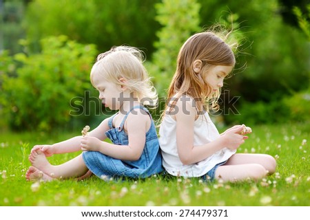 Two cute little sisters having fun while sitting on the grass on a sunny summer day
