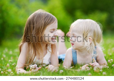 Two cute little sisters having fun while laying in the grass on a sunny summer day