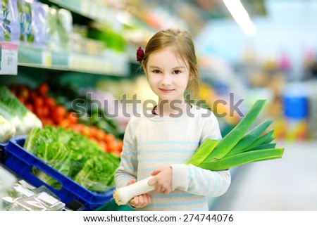 Little girl choosing a leek in a food store or supermarket