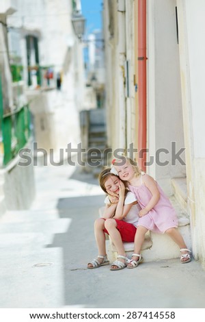 Two adorable little sisters laughing and hugging each other on warm and sunny summer day in Vieste, Italy