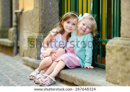 Two adorable little sisters laughing and hugging each other on warm and sunny summer day in italian town